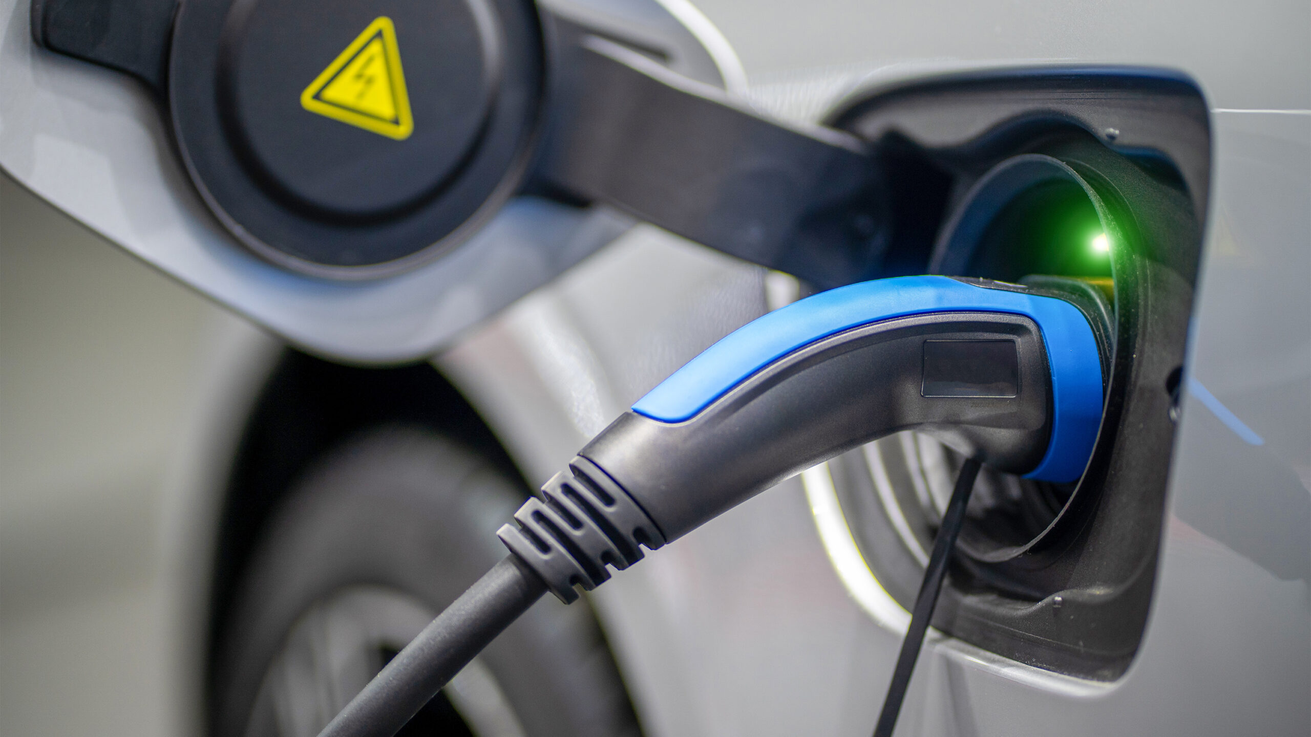 EV Car or Electric vehicle at charging station with the power cable supply plugged in on blurred nature with blue enegy power effect. 