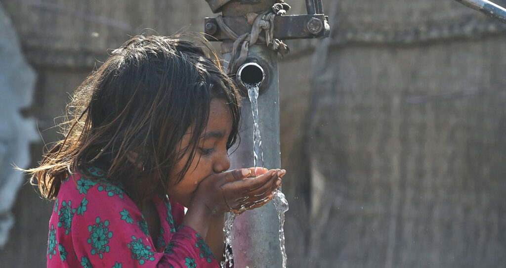 Girl drinking water from a hand water pump