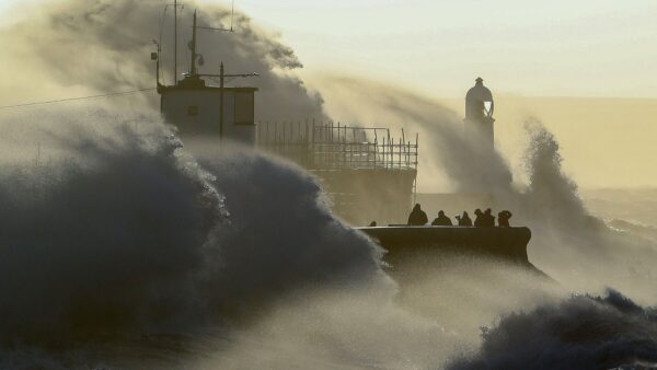 People watch as waves crash against the sea wall at Porthcawl, south Wales, on February 18, 2022 as Storm Eunice brings high winds across the country.